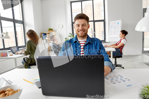 Image of smiling creative man with laptop working at office