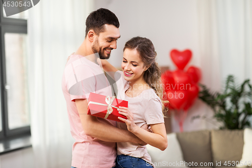 Image of happy couple with gift box hugging at home