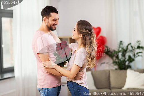 Image of happy couple with bunch of flowers hugging at home