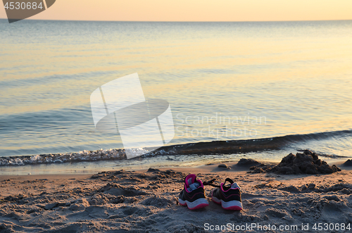 Image of Shoes by seaside on a beach by sunset