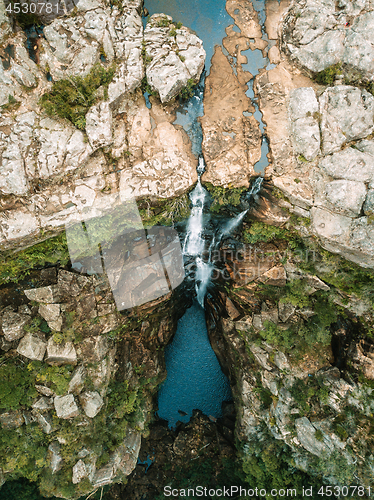 Image of Overhead views waterfall flowing into rock pool at base of cliff