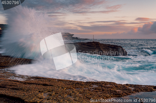 Image of Waves splash high onto the coastal rock shelf at sunrise