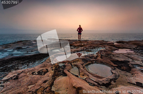 Image of Woman standing on sandstone rocks with foggy coastal sunrise