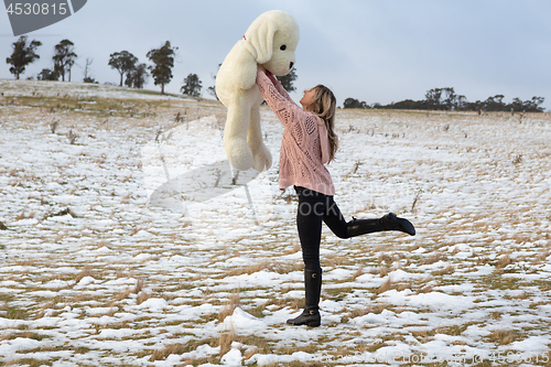 Image of Woman frolicking in the snow with teddy bear
