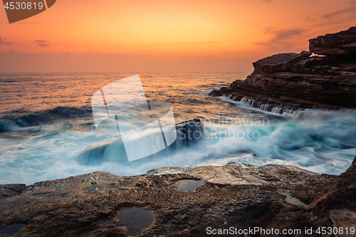 Image of Stunning sunrise and waves crash over rocks on the Sydney sea coast