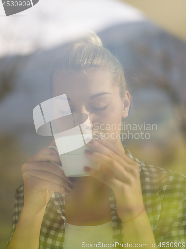 Image of young woman drinking morning coffee by the window