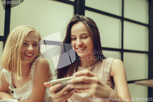 Image of Two girl friends spend time together drinking coffee in the cafe, having breakfast and dessert.