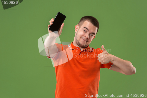 Image of The happy man showing at empty screen of mobile phone against green background.