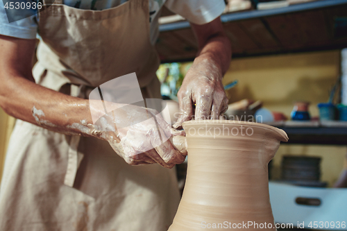 Image of Creating a jar or vase of white clay close-up. Master crock. Man hands making clay jug macro.