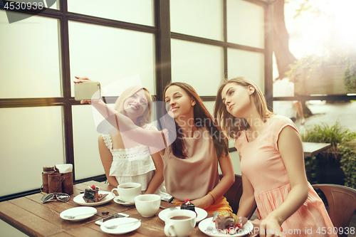 Image of Two girl friends spend time together drinking coffee in the cafe, having breakfast and dessert.