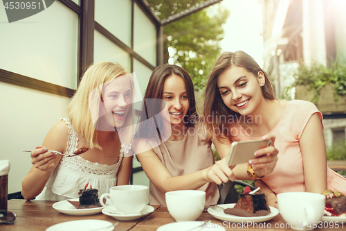 Image of Two girl friends spend time together drinking coffee in the cafe, having breakfast and dessert.