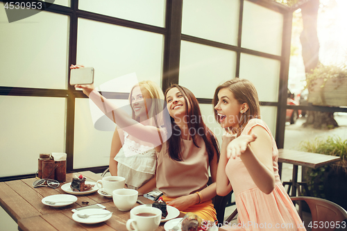 Image of Two girl friends spend time together drinking coffee in the cafe, having breakfast and dessert.