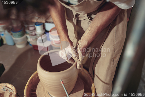 Image of Creating a jar or vase of white clay close-up. Master crock. Man hands making clay jug macro.