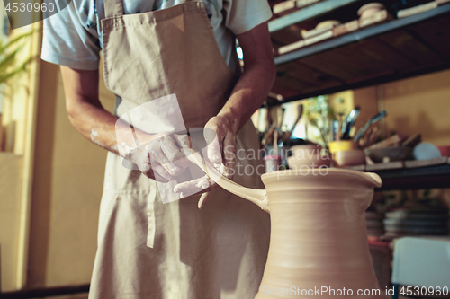 Image of Creating a jar or vase of white clay close-up. Master crock. Man hands making clay jug macro.