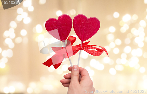 Image of close up of hand holding red heart shaped lollipop