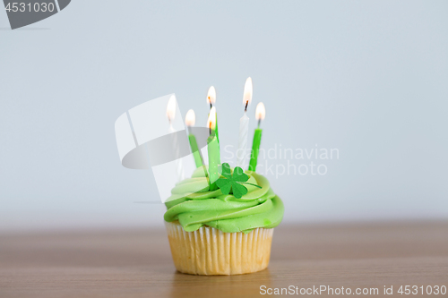 Image of green cupcake with six burning candles on table