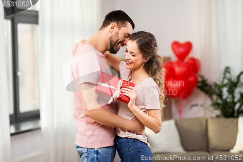 Image of happy couple with gift box hugging at home