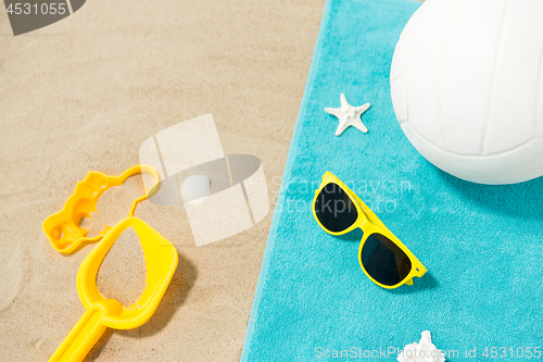 Image of sunglasses, sand toys and ball on beach towel