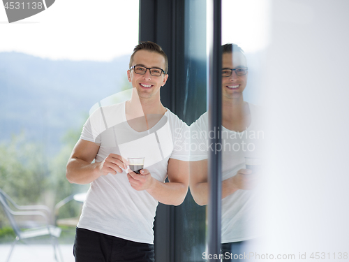 Image of young man drinking morning coffee by the window