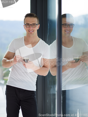 Image of young man drinking morning coffee by the window