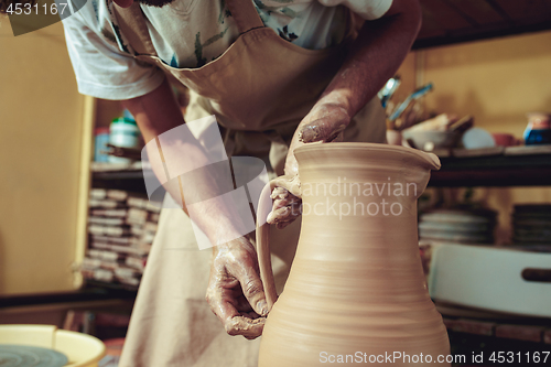 Image of Creating a jar or vase of white clay close-up. Master crock. Man hands making clay jug macro.