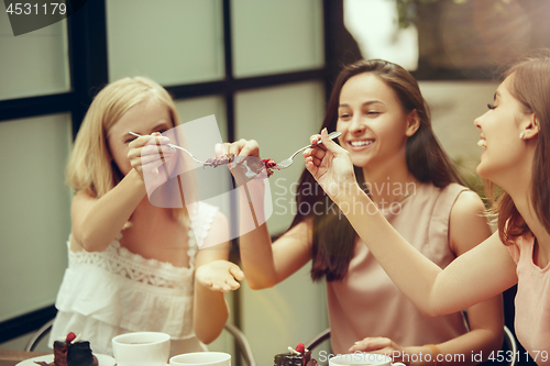 Image of Two girl friends spend time together drinking coffee in the cafe, having breakfast and dessert.