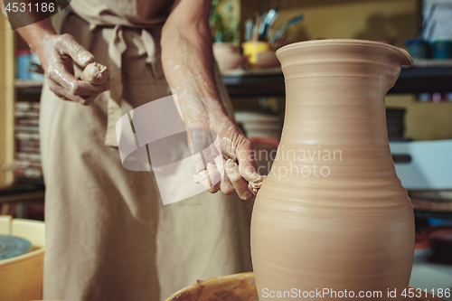 Image of Creating a jar or vase of white clay close-up. Master crock. Man hands making clay jug macro.