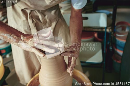 Image of Creating a jar or vase of white clay close-up. Master crock. Man hands making clay jug macro.