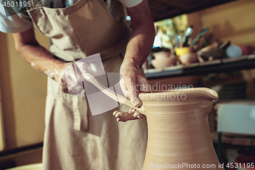 Image of Creating a jar or vase of white clay close-up. Master crock. Man hands making clay jug macro.