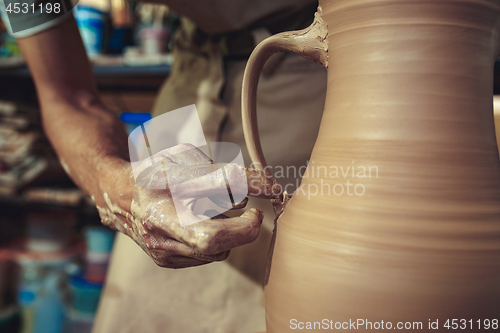 Image of Creating a jar or vase of white clay close-up. Master crock. Man hands making clay jug macro.