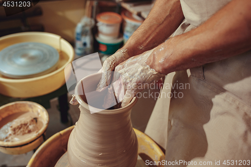 Image of Creating a jar or vase of white clay close-up. Master crock. Man hands making clay jug macro.