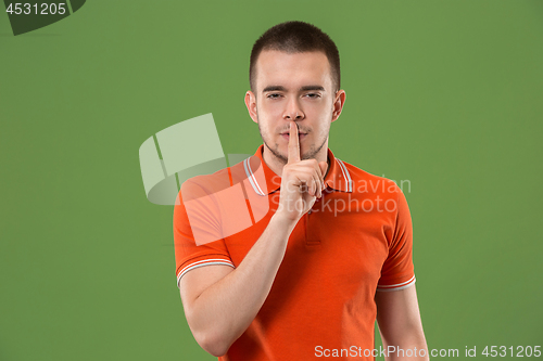 Image of The young man whispering a secret behind her hand over green background