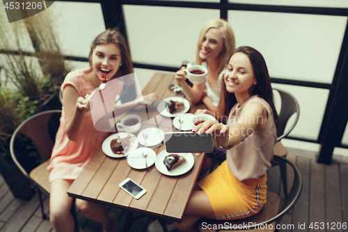 Image of Two girl friends spend time together drinking coffee in the cafe, having breakfast and dessert.