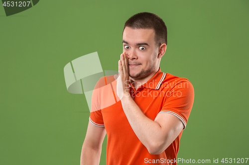 Image of The young man whispering a secret behind her hand over green background