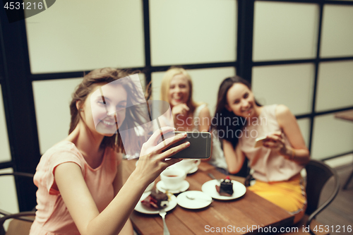 Image of Two girl friends spend time together drinking coffee in the cafe, having breakfast and dessert.