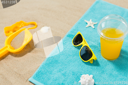 Image of sunglasses, sand toys and juice on beach towel