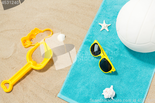Image of sunglasses, sand toys and ball on beach towel