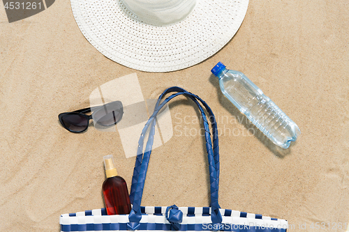 Image of beach bag, sunscreen, sunglasses and hat on sand