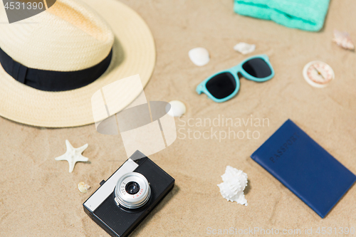 Image of camera, passport, sunglasses and hat on beach sand