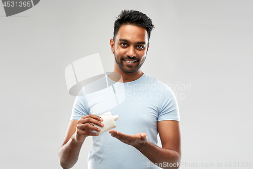 Image of happy indian man applying lotion to his hand