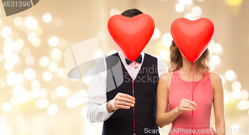 Image of couple hiding behind red heart shaped balloons