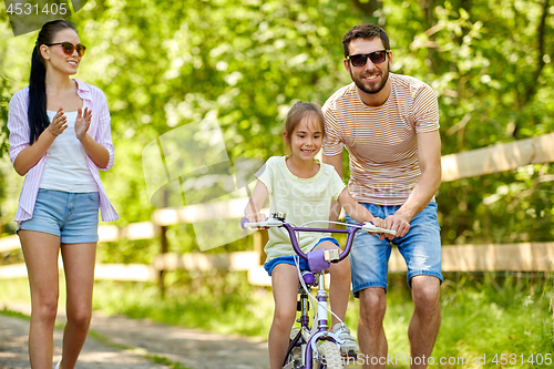 Image of kid with patents learning to ride bicycle in park