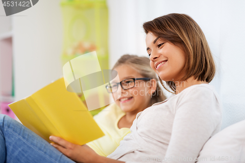 Image of happy girl with mother reading book at home