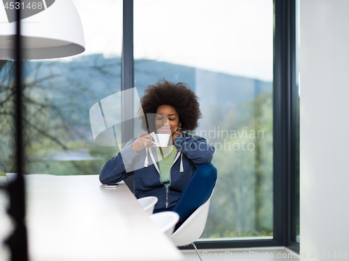 Image of black woman drinking coffee and using a mobile phone  at home