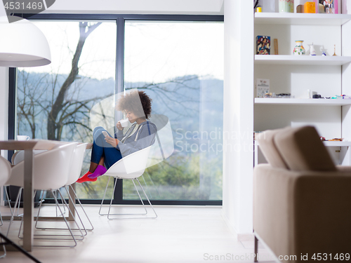 Image of black woman drinking coffee and using a mobile phone  at home