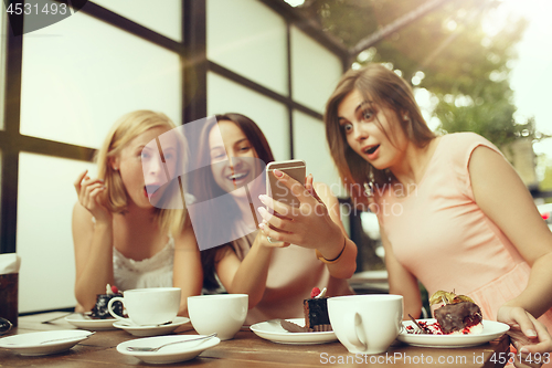 Image of Two girl friends spend time together drinking coffee in the cafe, having breakfast and dessert.