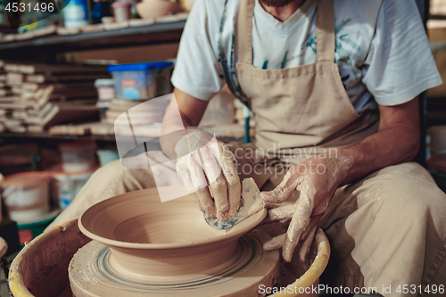 Image of Creating a jar or vase of white clay close-up. Master crock. Man hands making clay jug macro.