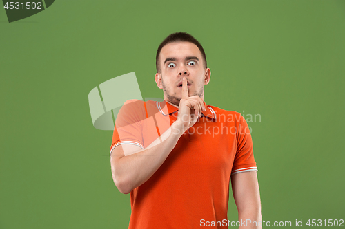 Image of The young man whispering a secret behind her hand over green background