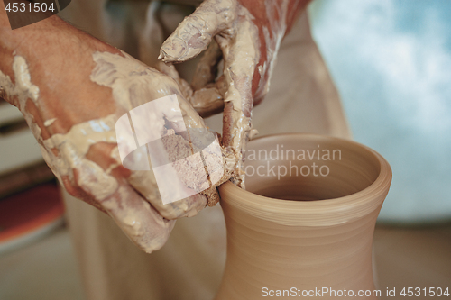 Image of Creating a jar or vase of white clay close-up. Master crock. Man hands making clay jug macro.