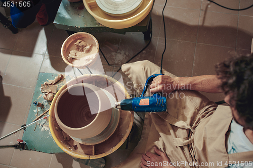 Image of Creating a jar or vase of white clay close-up. Master crock. Man hands making clay jug macro.